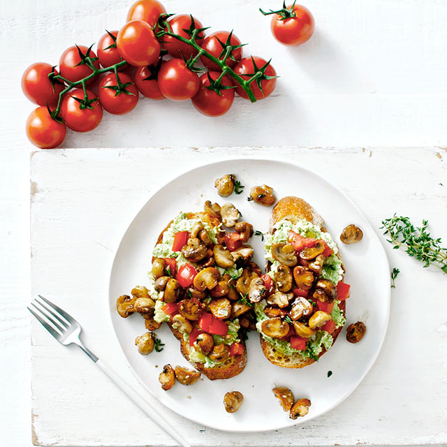Mushroom and avocado on toast sitting on a white table with some vine tomatoes next to it