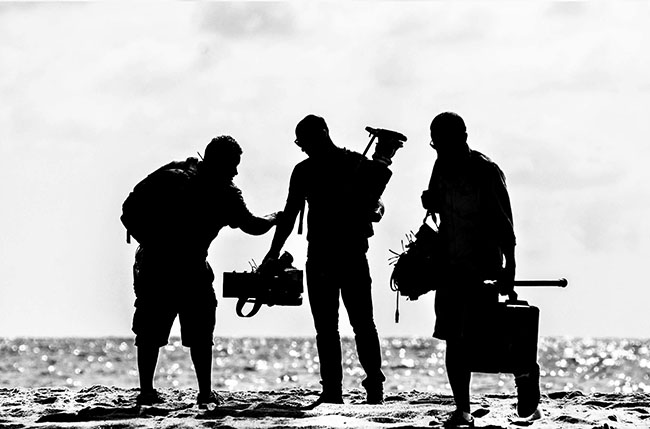 The men holding video equipment standing on a beach