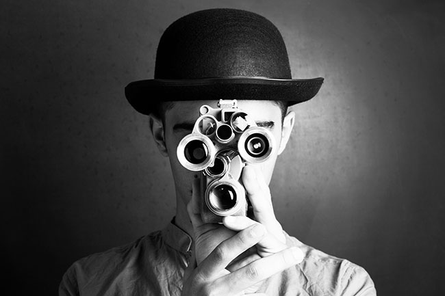 Black and white image of someone in a bowler hat holding a video camera and looking forward