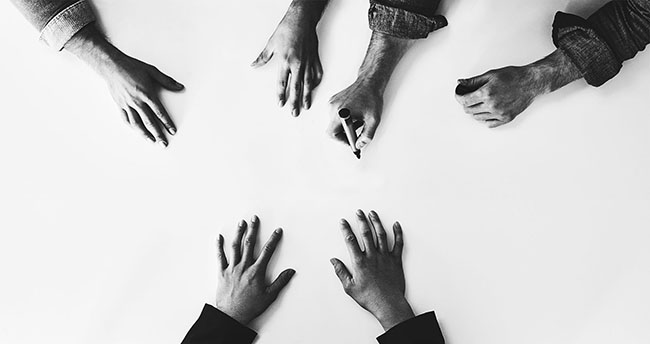 Overhead shot of a white background and 6 hands in the middle of the image