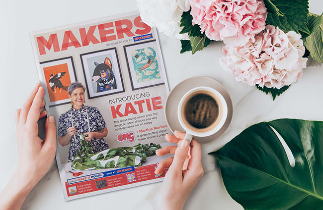 A magazine on a table next to a hand with a cup of coffee and some pink flowers 